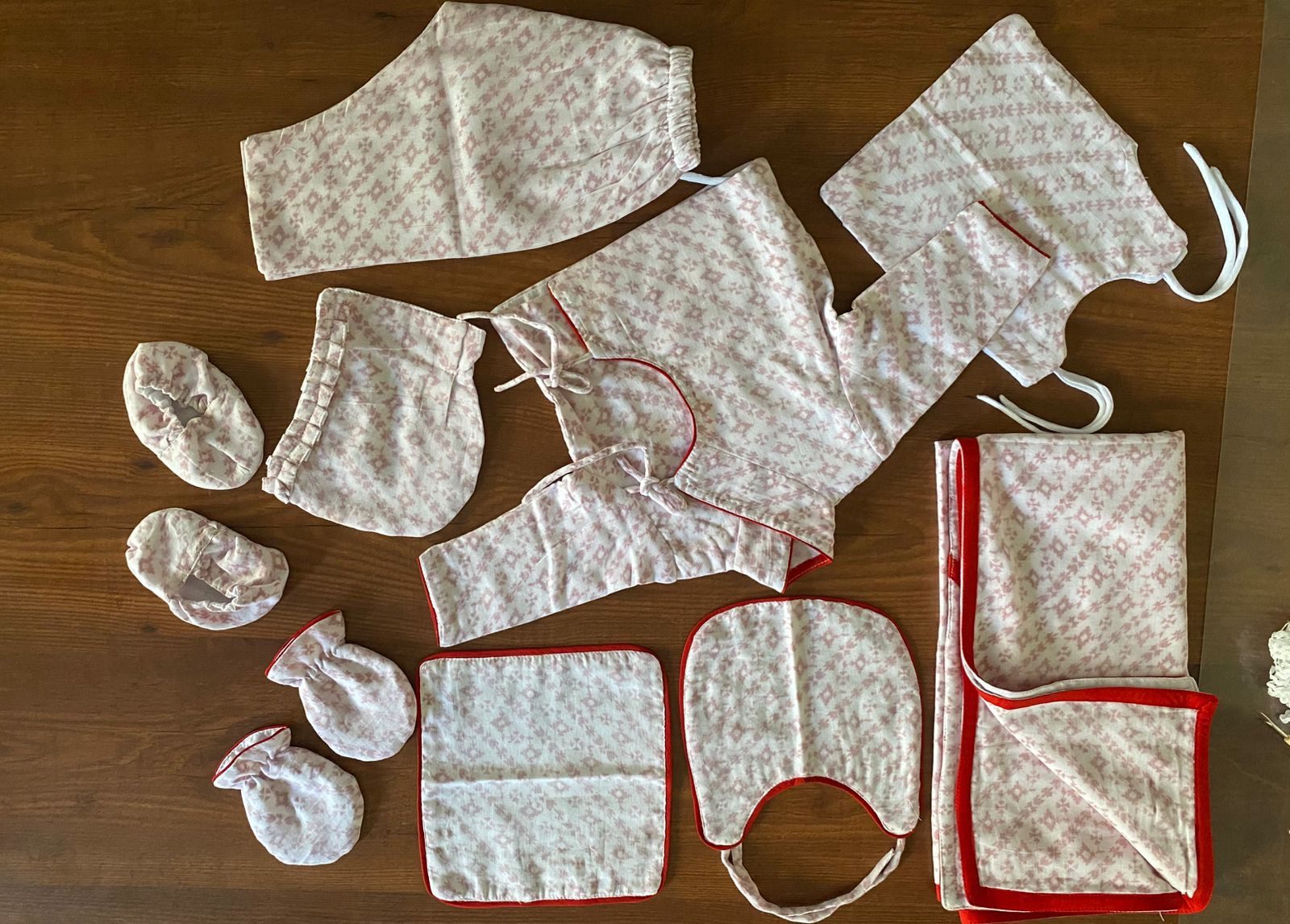 The complete Primula Baby Set laid out — pajamas, muslin cloths, caps, washcloths, gloves and booties in a soft rose Himalayan print